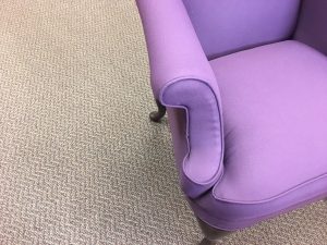 The arm of a purple upholstered chair.