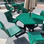 Multiple green metal picnic tables with green metal chairs.